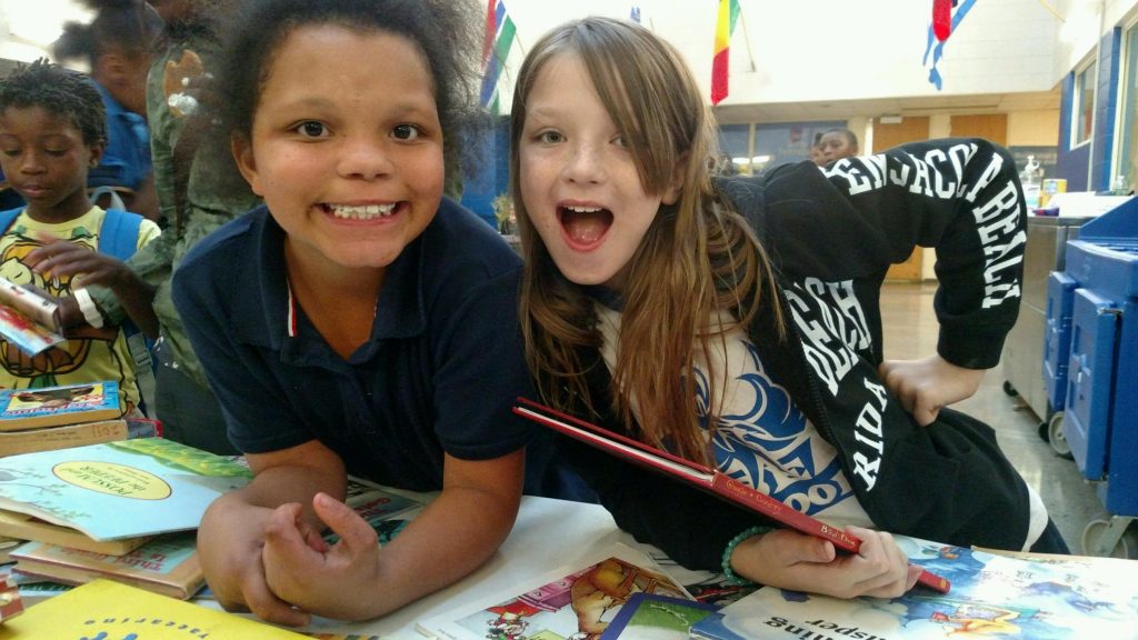 Two girls smiling with books from the Cleveland Kids' Book Bank at their after school arts program