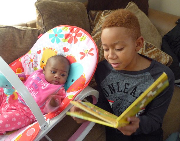 Boy reading book from the Cleveland Kids' Book Bank to his baby sister