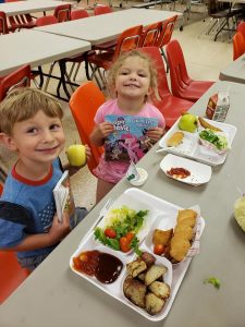 Boy and girl at a cafeteria table smiling at the camera