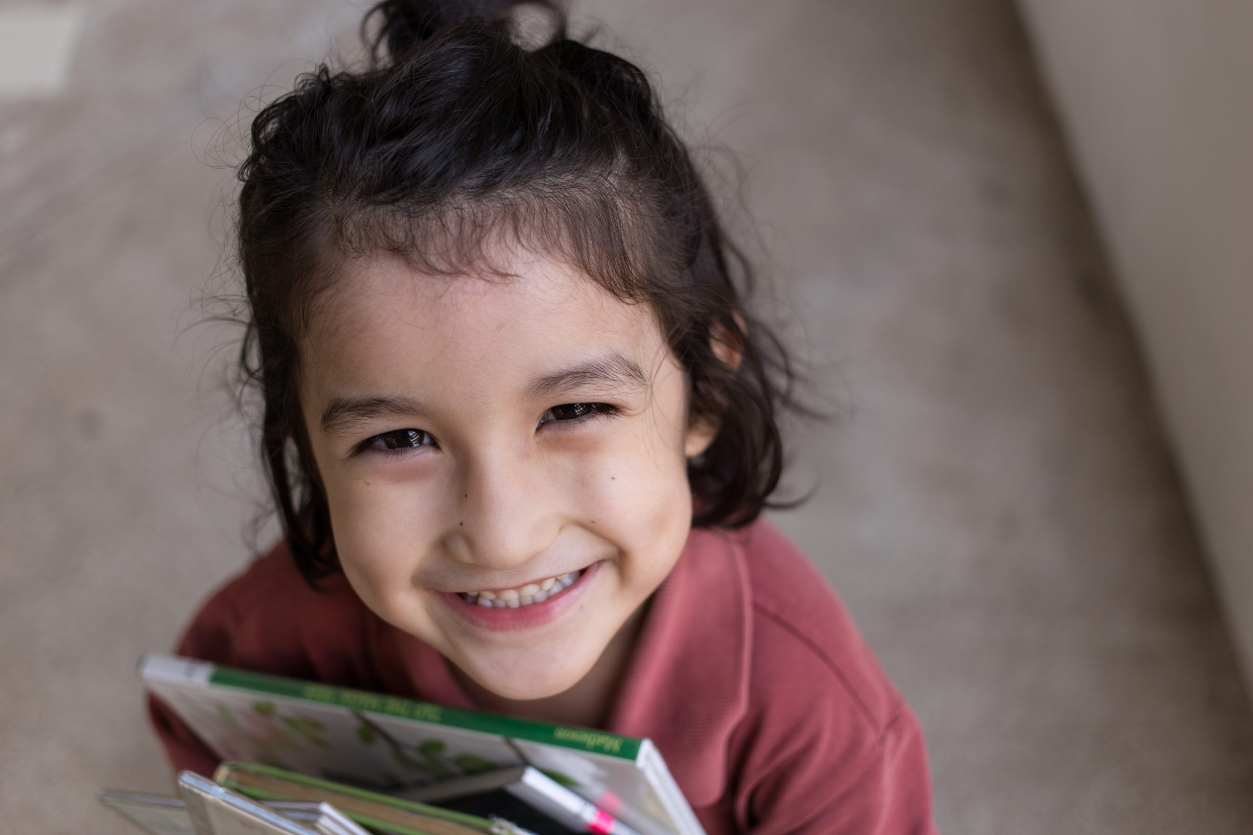 shutterstock_408195859 young girl with dark hair holding books and smiling