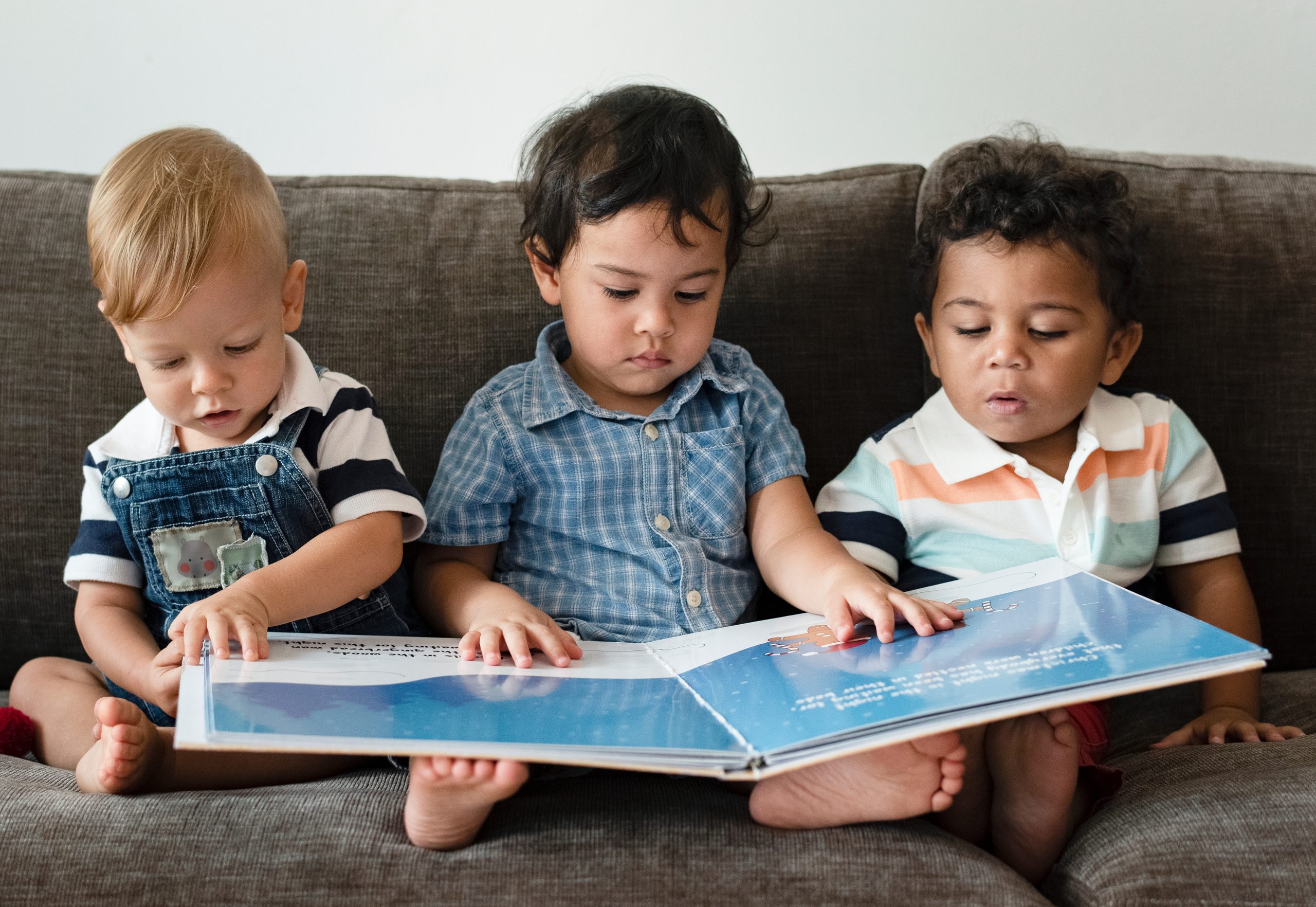 three boys sitting on a couch sharing a book