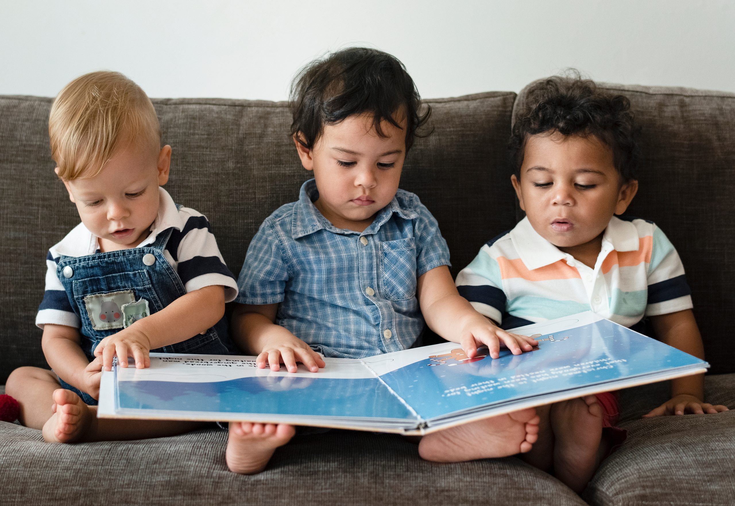 Three,Little,Boys,Reading,A,Book,On,A,Sofa three boys sitting on a couch sharing a book