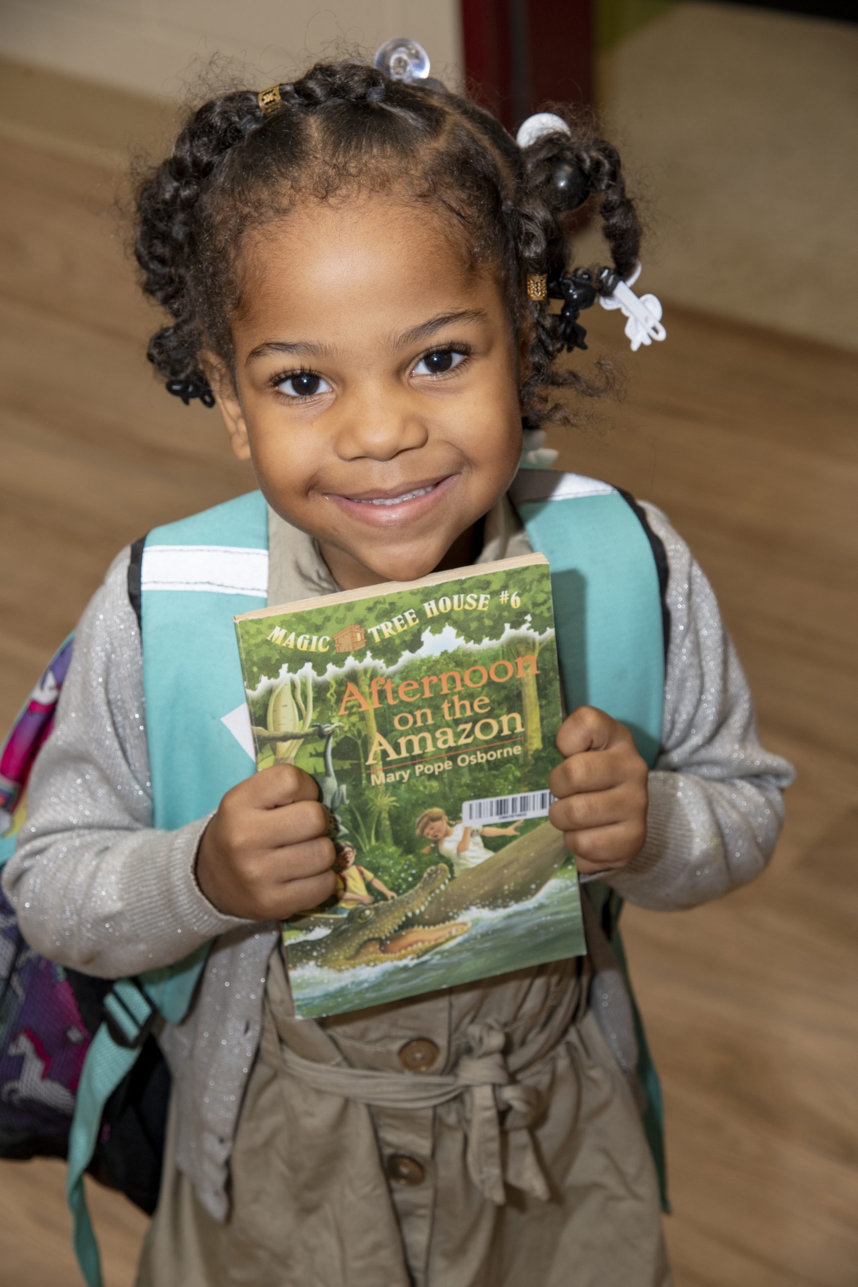 little girl with a backpack holding her copy of Magic Tree House in front of her