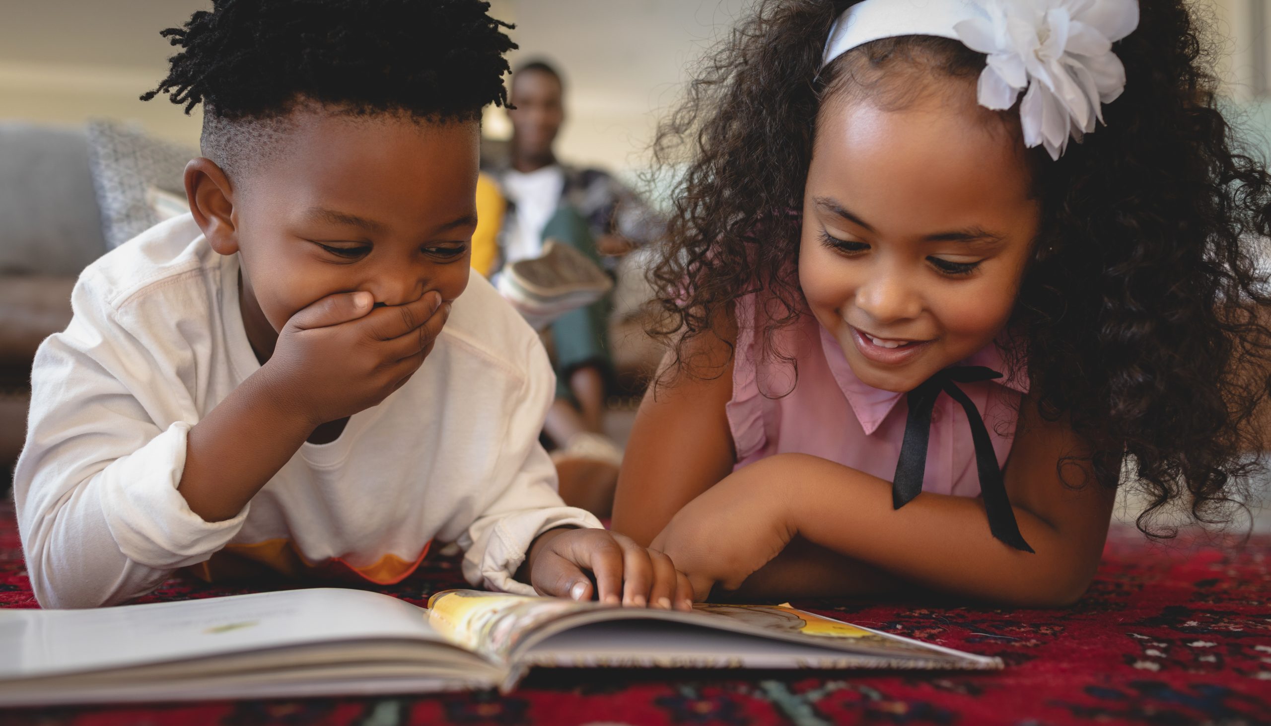 boy and girl laying on the ground reading a book together