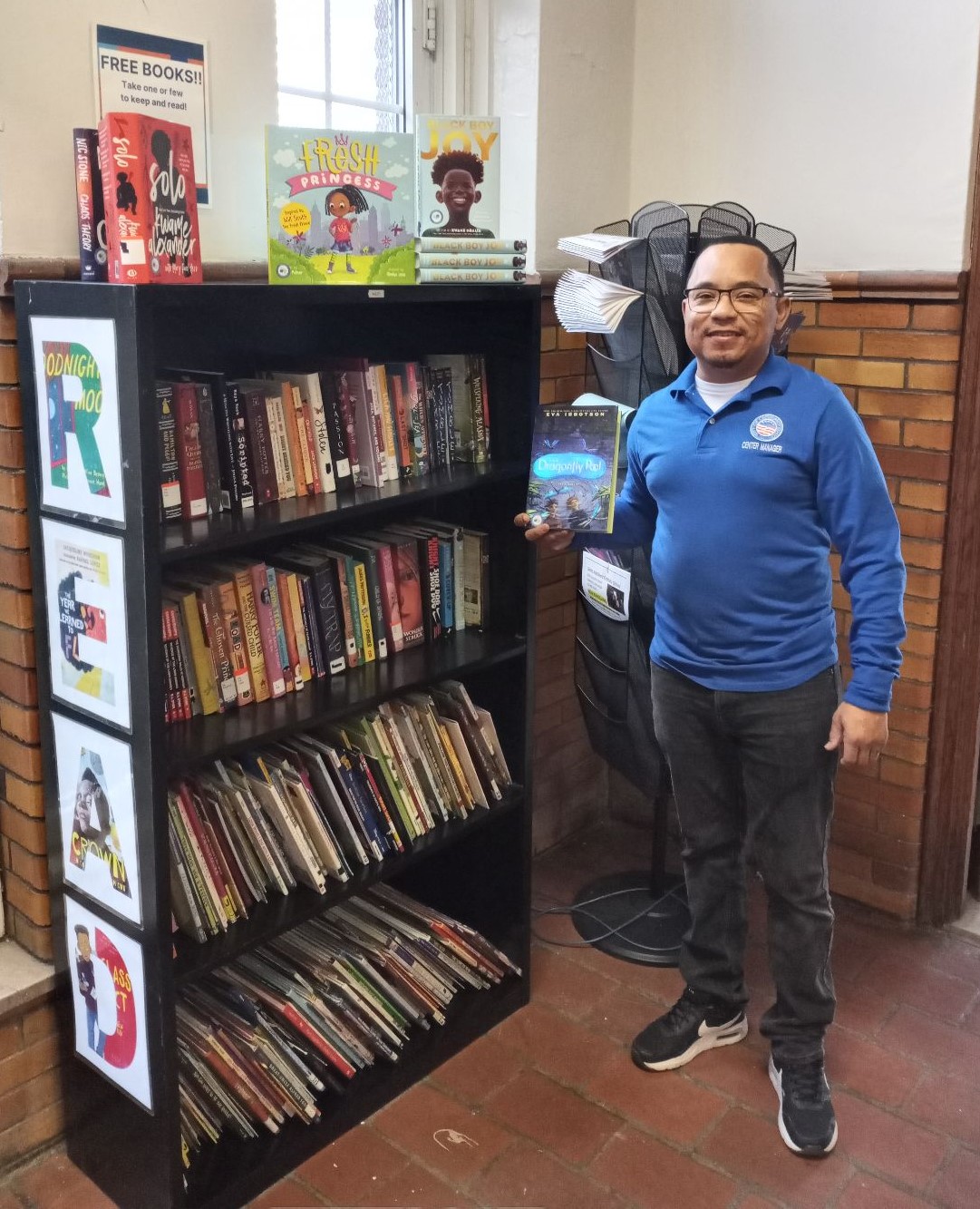 man in blue shirt standing next to a bookshelf full of books