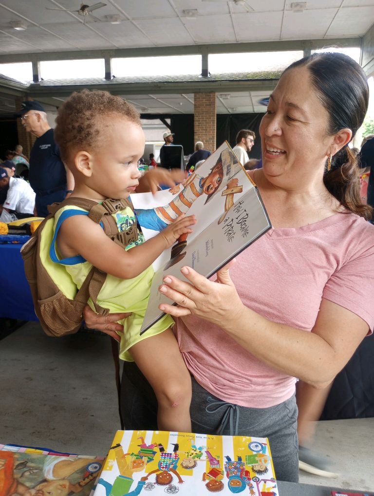 woman holding young child in her arms while showing him a book