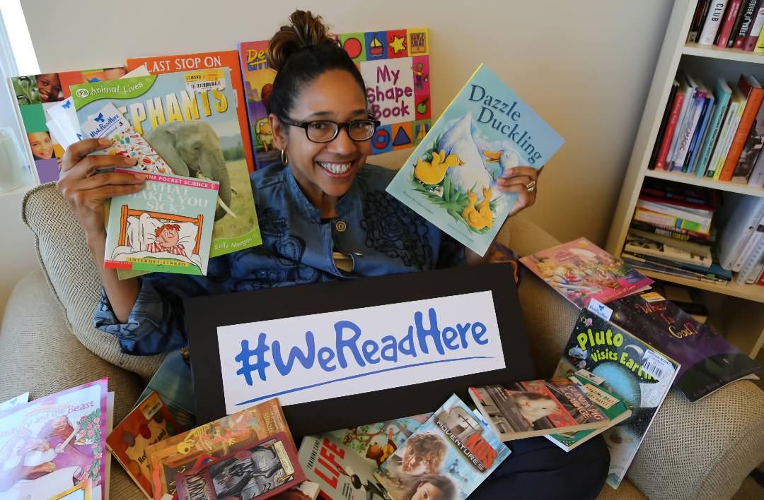 Woman with glasses sit on the floor surrounded by children's books